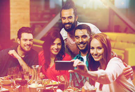 吃饭照片素材休闲,技术,友谊,人假日的快乐的朋友餐厅吃晚饭用智能手机自拍朋友们餐厅用智能手机自拍背景