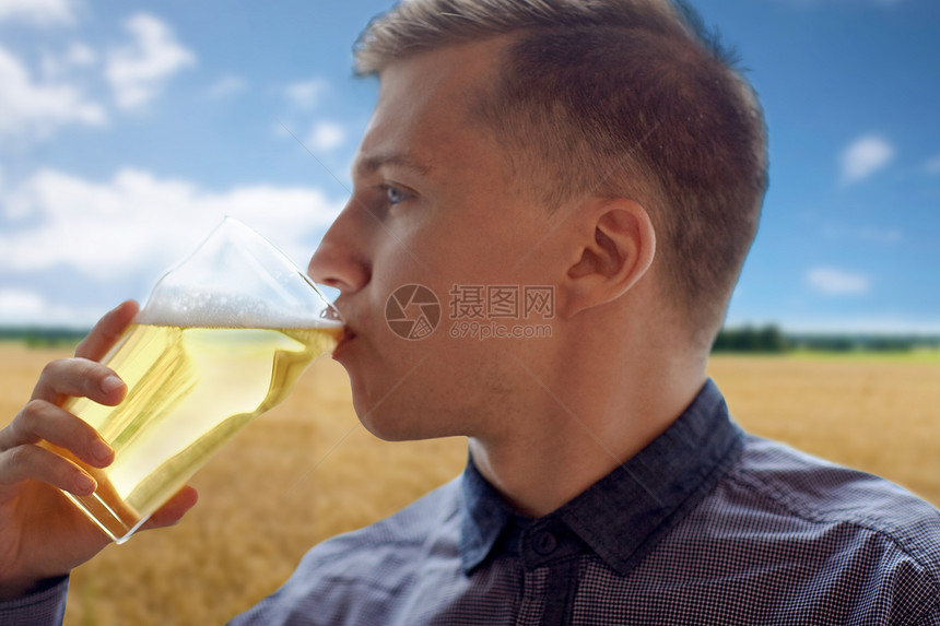 人,饮料,酒精休闲近距离的轻人喝啤酒璃谷类食品领域蓝天背景特写轻人璃上喝啤酒图片