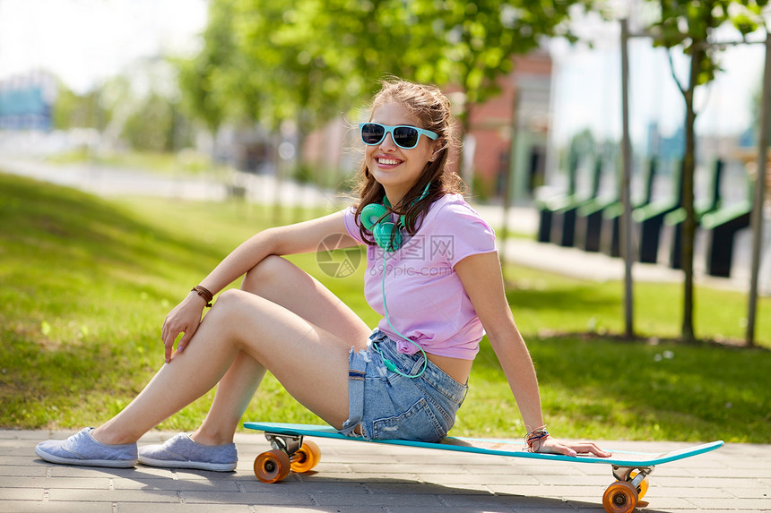 生活方式,休闲人们的微笑的轻妇女十几岁的女孩戴着太阳镜,戴着耳机坐公园的长板上带耳机长板的快乐少女图片