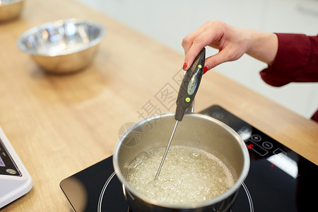 专业国外炖锅烹饪,食品厨房用具的厨师与温度计测量温度糖糖浆沸腾锅炉子上厨师厨房测量糖浆中的温度背景