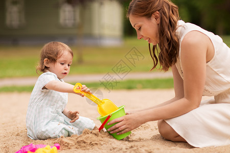 拎着水桶母亲在沙滩上陪孩子玩耍背景