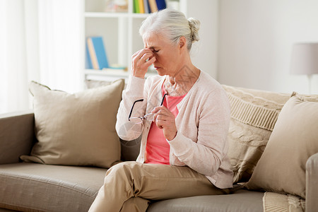 女头痛老健康问题老人戴着眼镜坐沙发上头痛背景