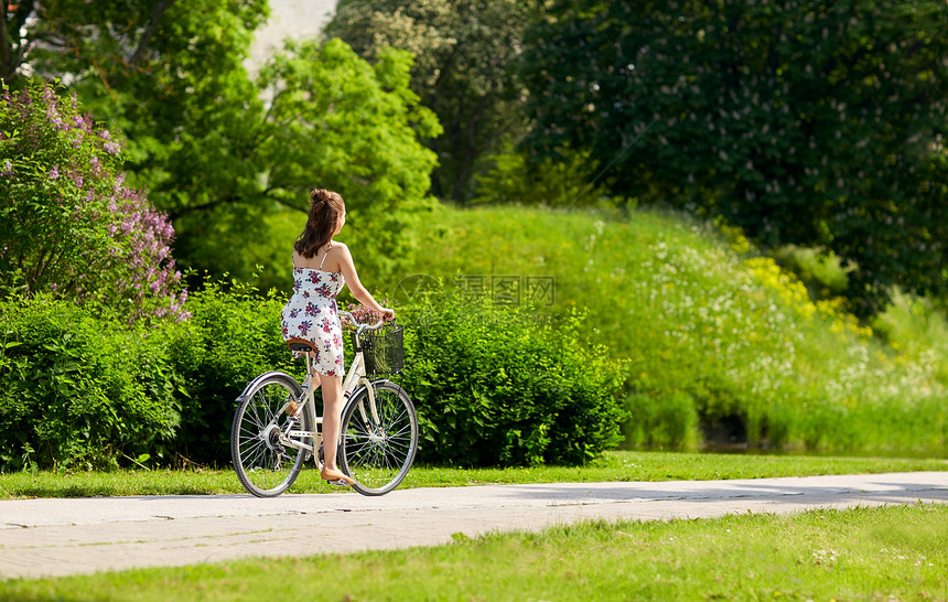 人们,休闲生活方式快乐的轻时髦女人穿着夏装,骑着固定自行车,公园的篮子里放着野花快乐的女人夏天的公园骑固定自行车图片