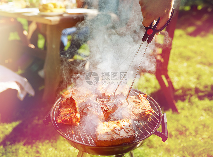 休闲,食物,人假日的男子烹饪肉烧烤为他的朋友夏季户外聚会夏天的聚会上,男人烧烤架上煮肉图片