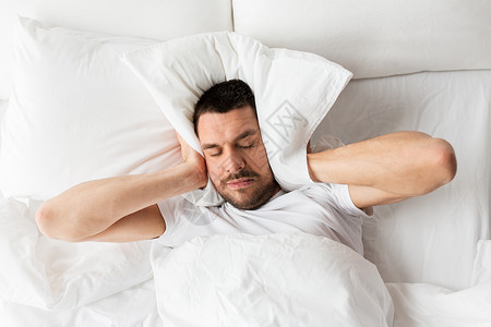 噪音监测人们,睡觉时间休息的男人躺床上,枕头家里被噪音所困扰男人躺床上,枕头上噪音背景
