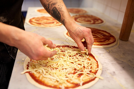 食物烹饪,烹饪人的厨师包师的手添加烤奶酪比萨饼店比萨店把磨碎的奶酪加比萨饼里饭背景图片