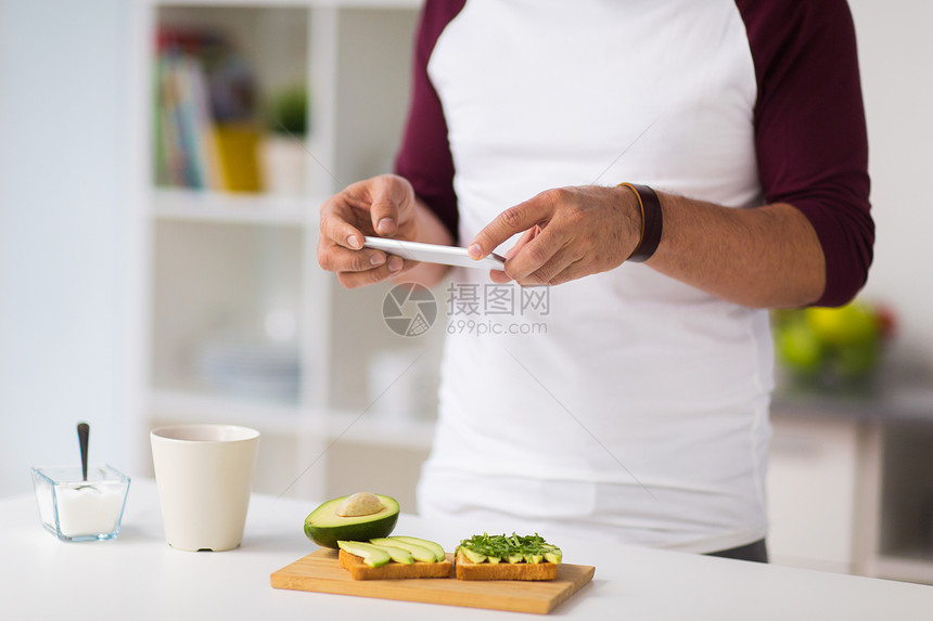 健康的饮食,人技术的男人智能手机吃早餐拍摄蔬菜三明治家里厨房男人家用智能手机拍摄食物图片