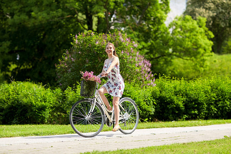 人们,休闲生活方式快乐的轻时髦女人穿着夏装,骑着固定自行车,公园的篮子里放着野花快乐的女人夏天的公园骑固定自行车背景图片