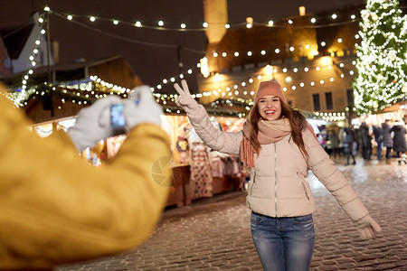 节日,冬天人们的快乐的女人诞节市场的广场上用智能手机为男朋友摆姿势快乐的女人诞节为智能手机摆姿势背景图片
