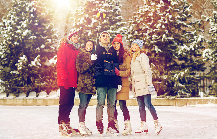 人友谊技术休闲理念快乐的朋友户外滑冰场上用智能手机自拍杆拍照滑冰场上智能手机的快乐朋友图片