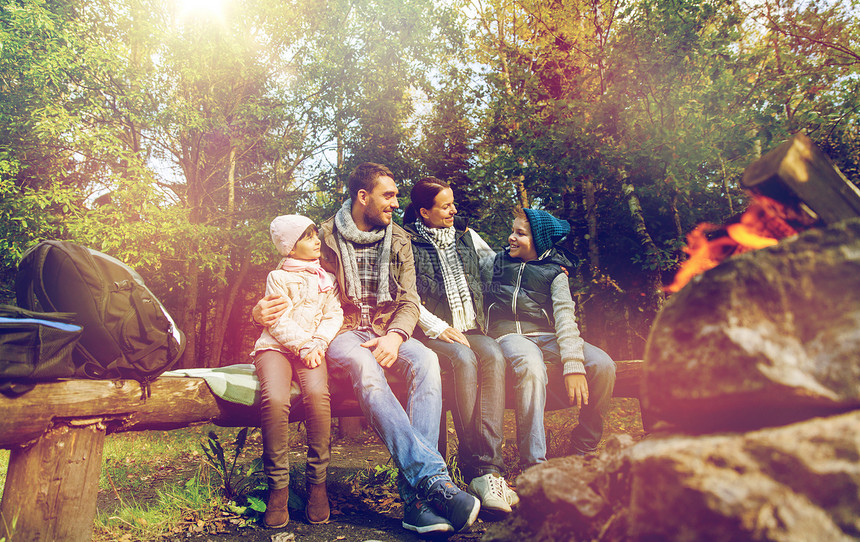 徒步旅行,旅游人们的快乐的家庭坐长凳上,森林篝火附近的营地交谈幸福的家庭坐篝火旁的长凳上图片