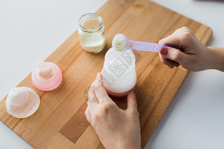 食物营养母亲手与婴儿瓶铲子准备婴儿配方奶用瓶子勺子制作配方牛奶背景图片