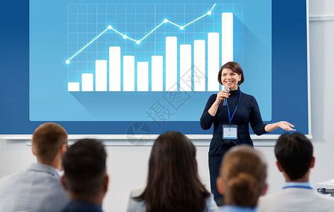 导师讲座商业,统计人的微笑的女商人讲师与麦克风图表投影屏幕上与学生会议演讲讲座出席商务会议讲座的群人背景