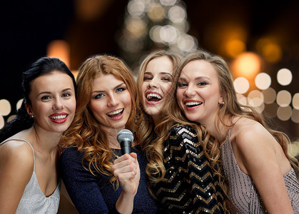 节日人们的快乐的女人与麦克风唱卡拉OK新聚会上的诞树灯光背景女人诞节用麦克风唱卡拉OK背景图片