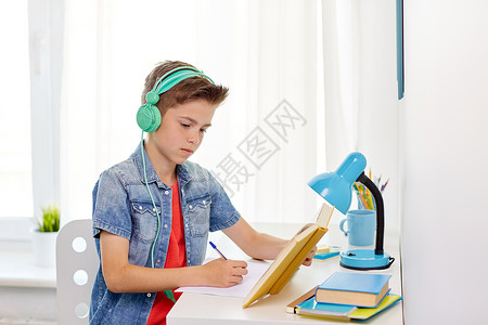 音乐教材教育,童人的快乐的学生男孩戴着耳机,家里的书笔记本学生男孩戴着耳机写笔记本上背景