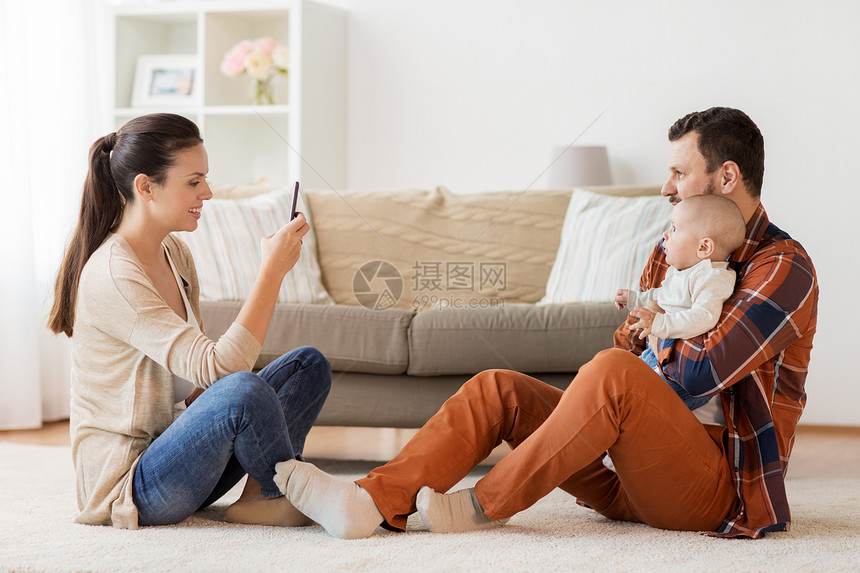 家庭,父母人的快乐的母亲与智能手机拍照的父亲与婴儿家里幸福的家庭婴儿家里拍照图片