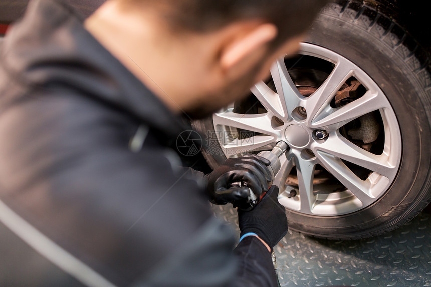 汽车服务,维修,维护人的汽车技工与电动螺丝刀更换轮胎车间汽车机械师与螺丝刀更换汽车轮胎图片
