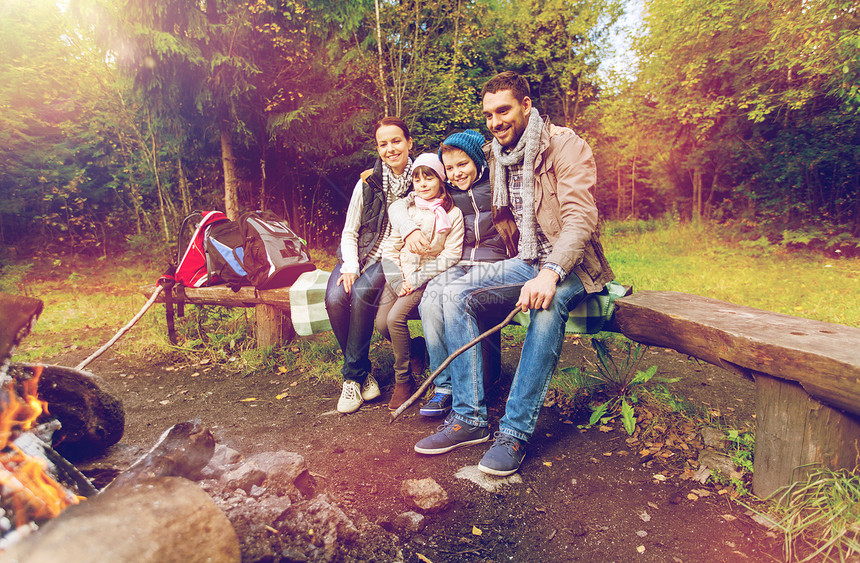 野营,旅游,旅游徒步旅行的快乐的家庭坐长凳上,森林篝火附近的营地交谈幸福的家庭坐篝火旁的长凳上图片