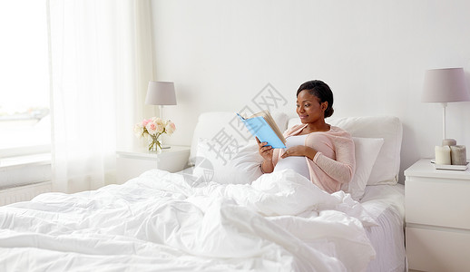 怀孕休闲微笑怀孕的非裔美国妇女家床上看书快乐的怀孕非洲妇女家看书图片