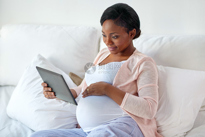 怀孕,技术,人期望快乐的怀孕非裔美国妇女与平板电脑电脑床上家快乐的孕妇家里用平板电脑图片