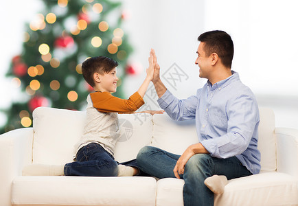 家庭,手势人的快乐的父子家里高五诞树背景快乐的父子诞节高五图片