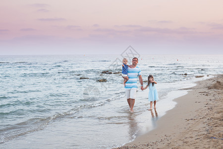 轻的父亲他的两个漂亮的孩子晚上沿着沙滩散步空荡荡的海滩上散步图片