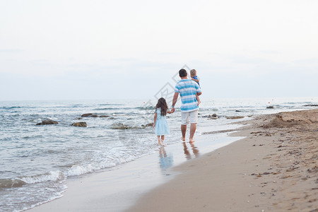 傍晚时分,轻的父亲他的两个漂亮的孩子沿着沙滩散步空荡荡的海滩上散步图片