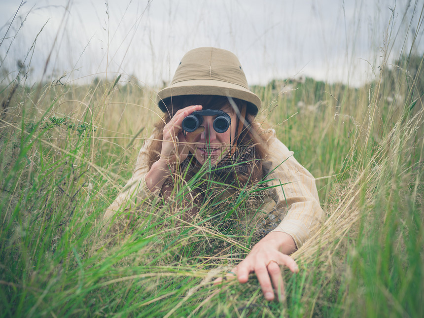 个戴着狩猎帽的轻女人躲高高的草丛里,正用望远镜看图片