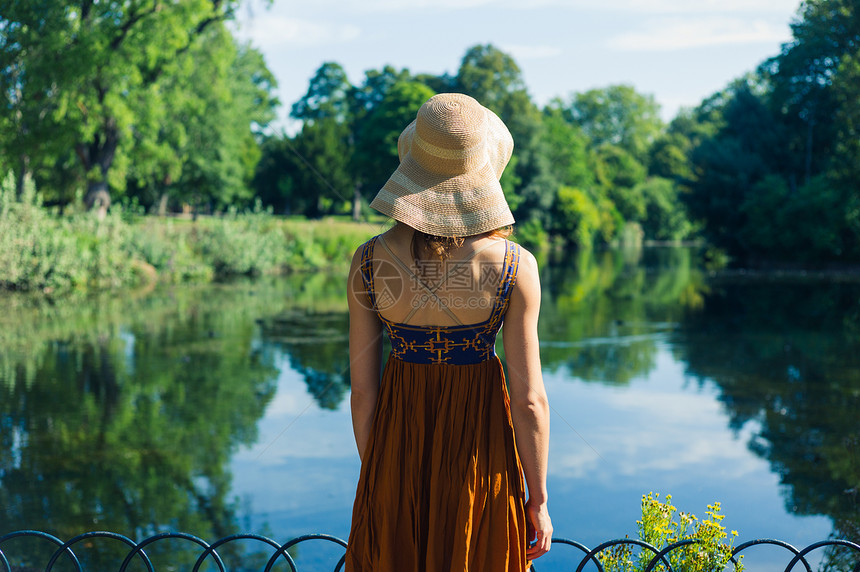 个轻的女人穿着连衣裙帽子站公园的池塘边,个阳光明媚的夏天图片
