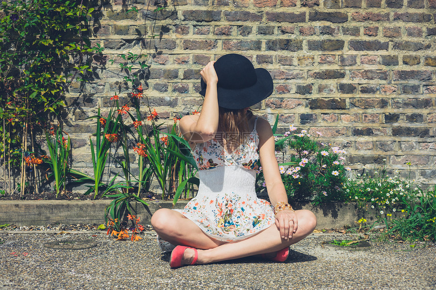个穿着夏装帽子的轻女人坐外的砖墙花坛旁图片