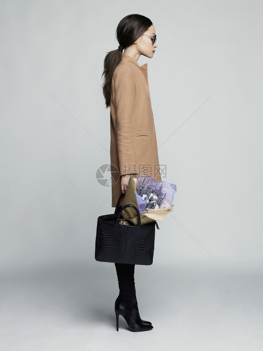 时尚工作室照片轻时尚的女人米色外套,黑色皮靴袋子,薰衣草花目录衣服看书图片