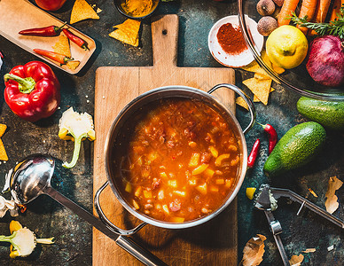墨西哥素食豆汤烹饪锅与瓢乡村厨房桌子配料切割板,顶部视图素食素食健康食品背景图片