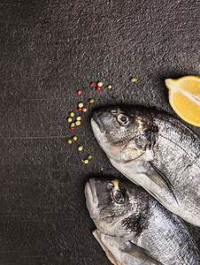 两个生多拉多鱼头与柠檬胡椒黑色的石头背景,图片