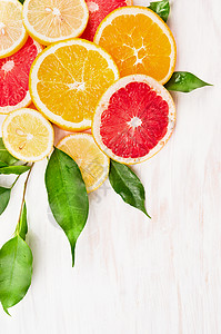 彩色柑橘类水果切片,白色木质背景上绿叶,角边图片