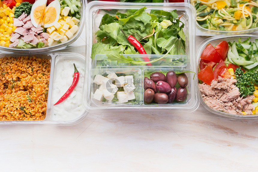 各种健康沙拉碗塑料包装的饮食午餐白色木制背景,顶部视图图片