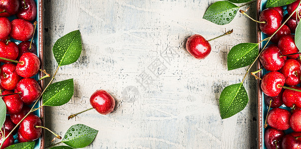 红色甜樱桃背景与绿叶白色木制背景,顶部视图,框架图片