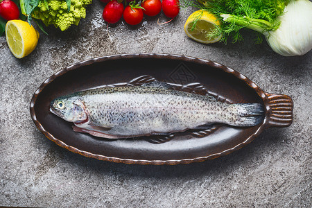 生鲜全鳟鱼烤盘与蔬菜烹饪配料灰色混凝土背景,顶部视图健康食品的图片
