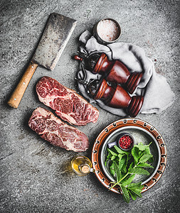 生鲜大理石牛排与肉刀调味料黑暗的乡村混凝土背景,顶部的肉类烹饪准备图片