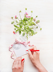 女手白色木制背景上写张贺卡,花粉红色丝带,视图,模拟图片
