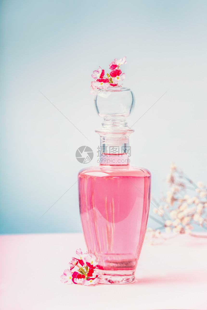 瓶带粉红色花朵的乳液香水,天然化妆品美容,背景为淡蓝色,正图片