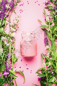 粉红色青蛙罐子天然草药护肤美容璃罐与奶油乳液新鲜草药花卉粉红色背景,顶部视图,垂直美容,皮肤头发护理的背景