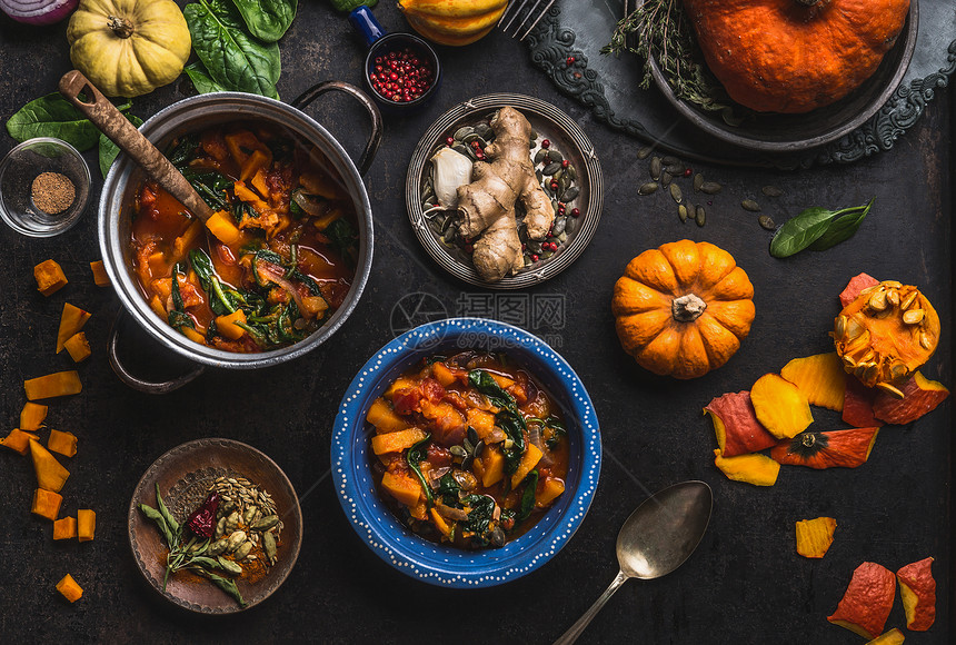 纯素南瓜炖菜与菠菜碗与勺子黑暗的厨房桌子背景与锅配料健康的季节食物干净的饮食观念图片
