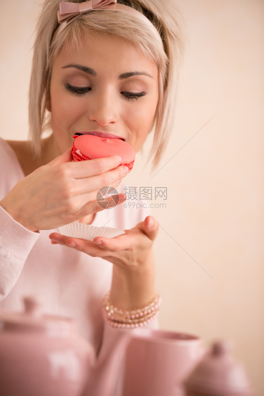 轻漂亮的金发女人喝茶的时候吃马卡龙她很满意短发粉红色现代风格图片