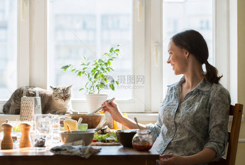 女人家煮披萨用配料填充,而猫则窗户上放松图片