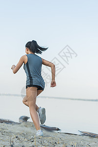 轻的女士早上海滩上跑步高清图片