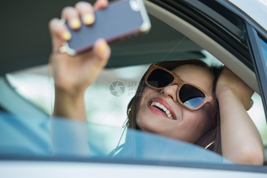 假期旅游微笑的十几岁女孩汽车户外用智能手机相机自拍图片