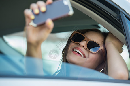 假期旅游微笑的十几岁女孩汽车户外用智能手机相机自拍图片