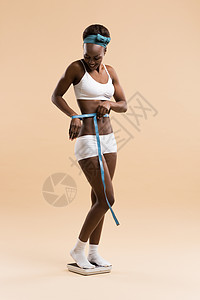 非洲妇女站秤上测量腰部,用胶带庆祝减肥健康的身体图片
