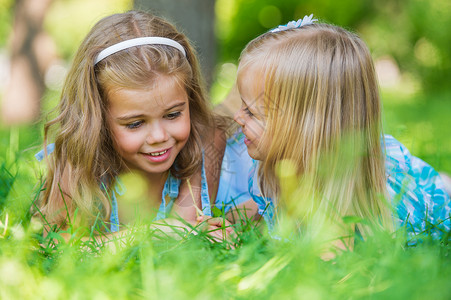 两个小妹妹夏天的公园里玩得很开心,边躺草坪上背景图片