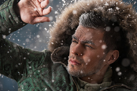 冬天的雪中,英俊的男人穿着带毛皮帽的夹克图片